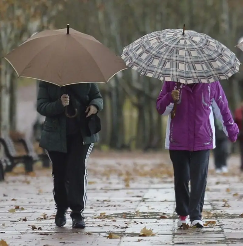 Dos mujeres pasean por Valladolid protegiéndose con paraguas de la lluvia