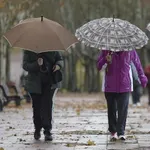 Dos mujeres pasean por Valladolid protegiéndose con paraguas de la lluvia
