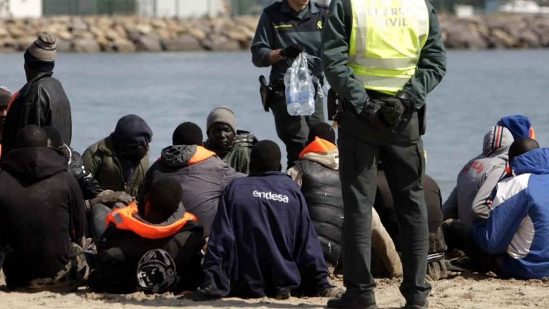 Dos miembros de la Guardia Civil junto al grupo de 25 inmigrantes que han llegado a bordo de una patera hoy a la playa de San Lorenzo de Melilla