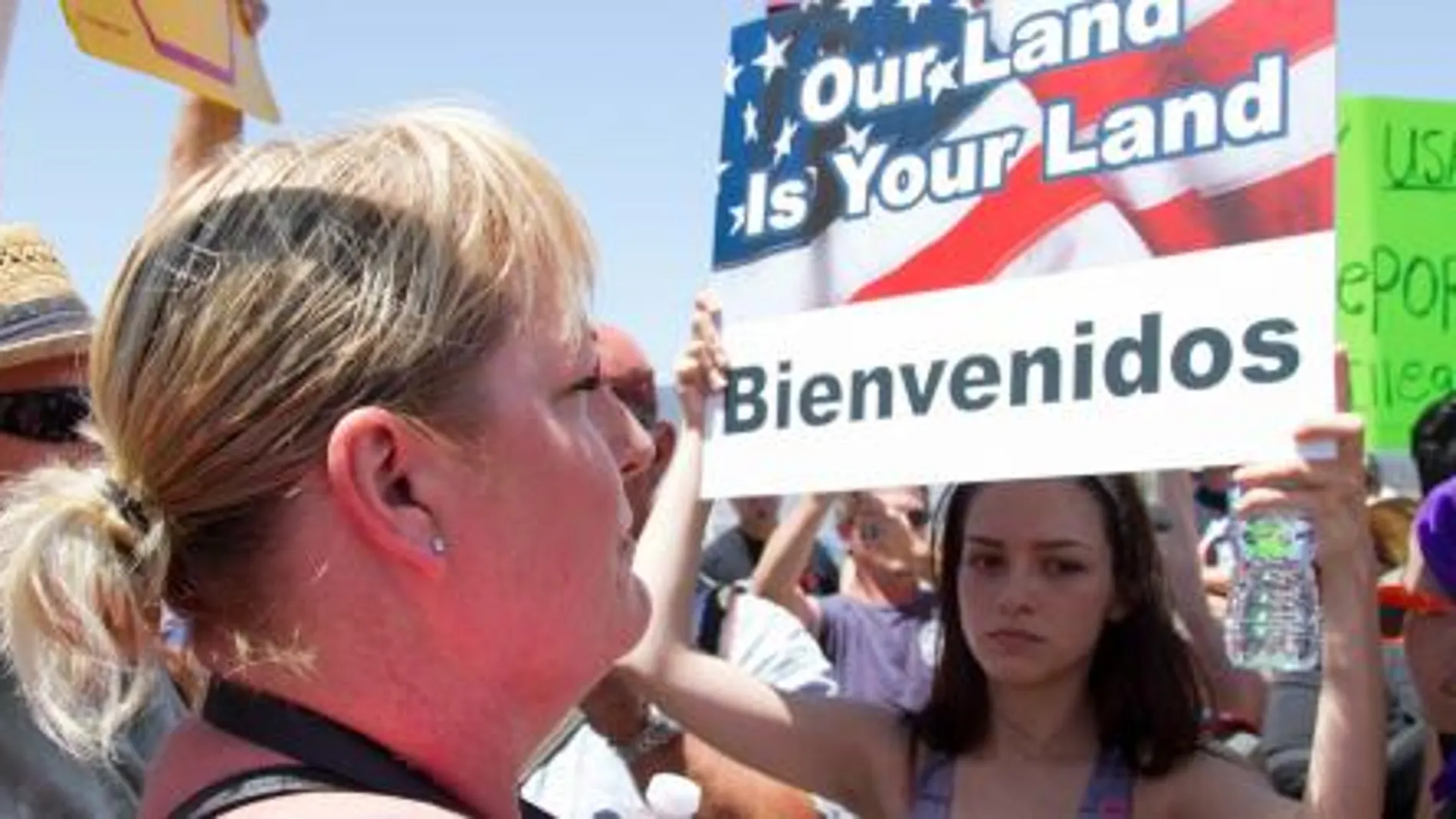 Una mujer sostiene un letrero que dice: "Nuestra tierra es tu tierra. Bienvenidos"durante una manifestación hoy, viernes 4 de julio 2014, frente al Centro de Procesamiento de La Patrulla Fronteriza en Murrieta, California (EE.UU.).