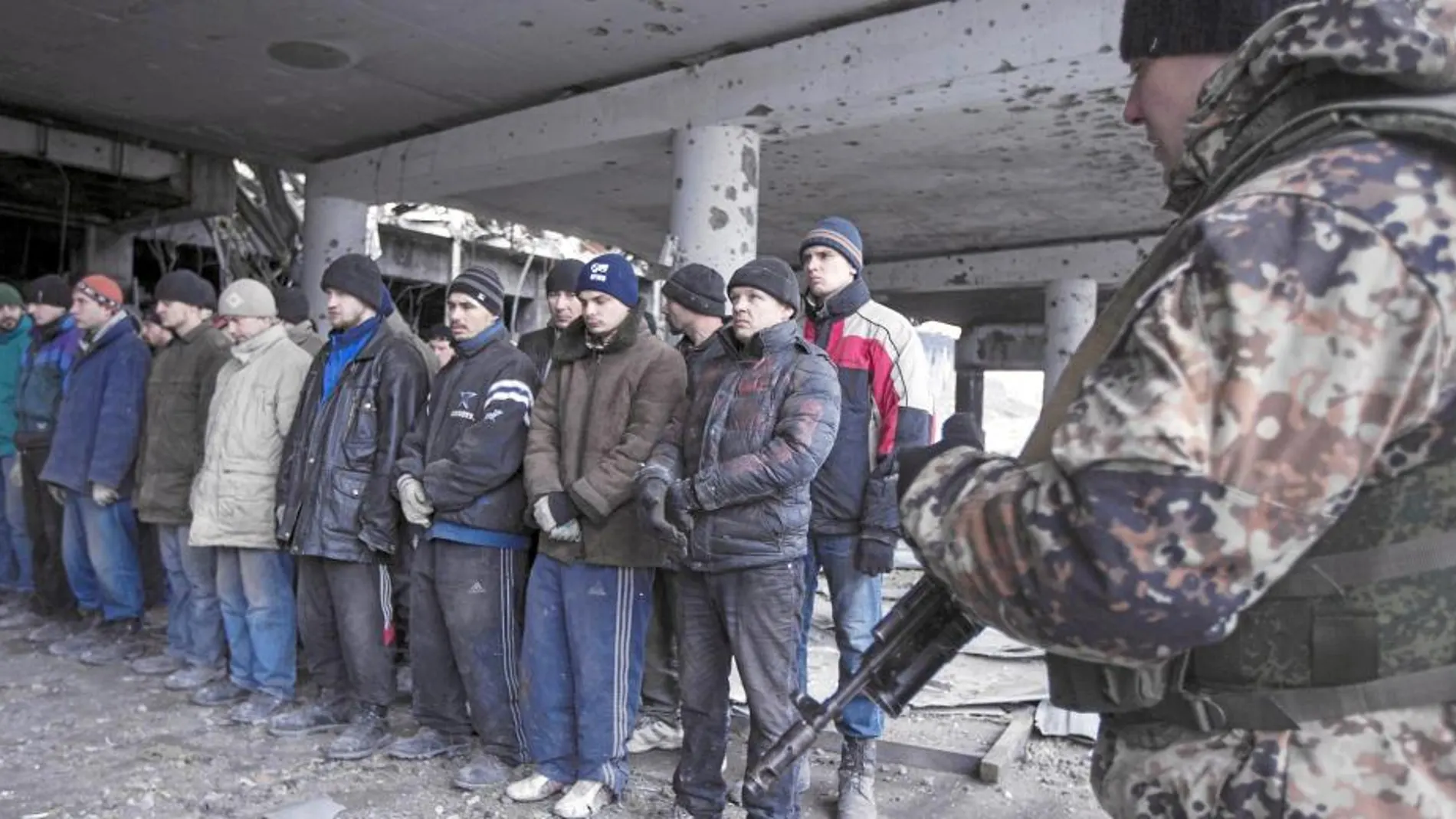 Un miliciano secesionista vigila a un grupo de prisioneros de guerra ucranianos en el aeropuerto de Donetsk