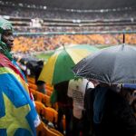 Un sudafricano se envuelve en una bandera para protegerse de la intensa lluvia caída durante el multitudinario servicio religioso oficial