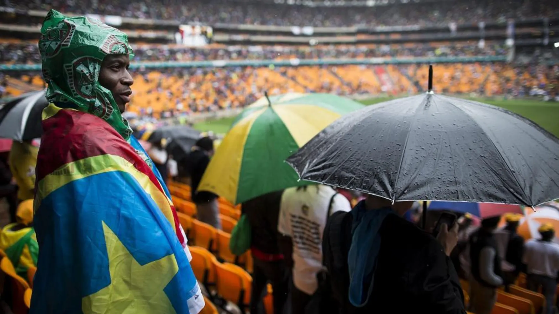 Un sudafricano se envuelve en una bandera para protegerse de la intensa lluvia caída durante el multitudinario servicio religioso oficial