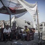 Tres palestinos descansan sentados en un sofá a la entrada de su casa destruida en el barrio de Shujaiya, al este de la ciudad de Gaza
