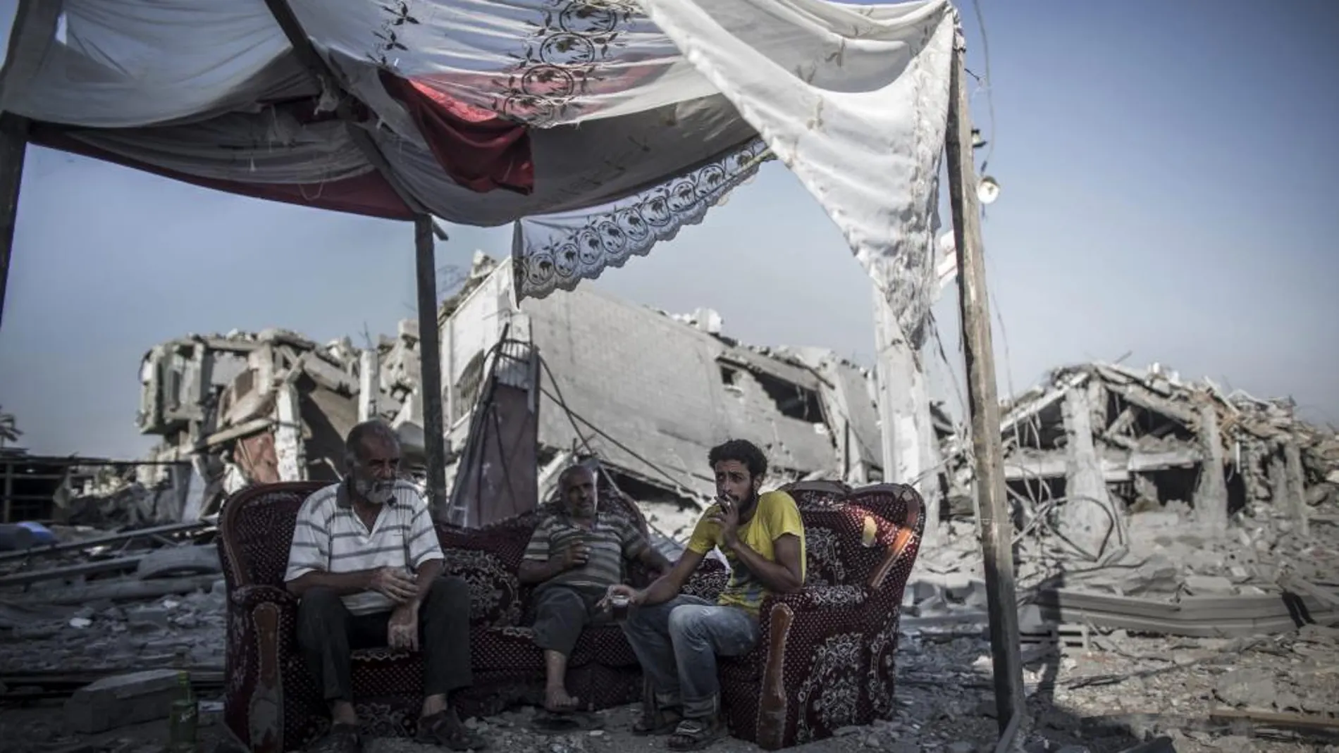 Tres palestinos descansan sentados en un sofá a la entrada de su casa destruida en el barrio de Shujaiya, al este de la ciudad de Gaza