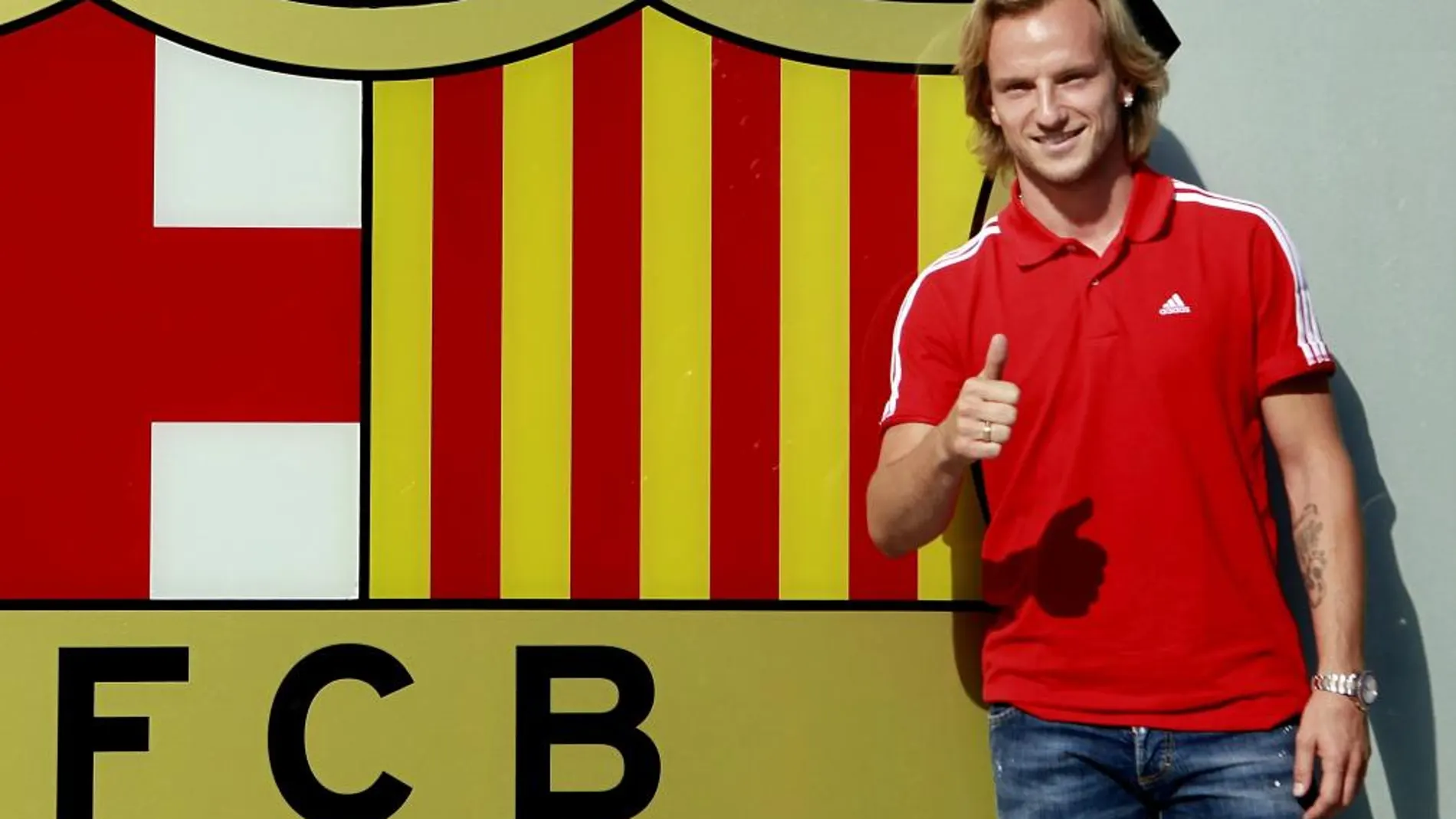 El centrocampista croata Ivan Rakitic posa esta tarde junto al escudo que preside la entrada de las oficinas del FC Barcelona