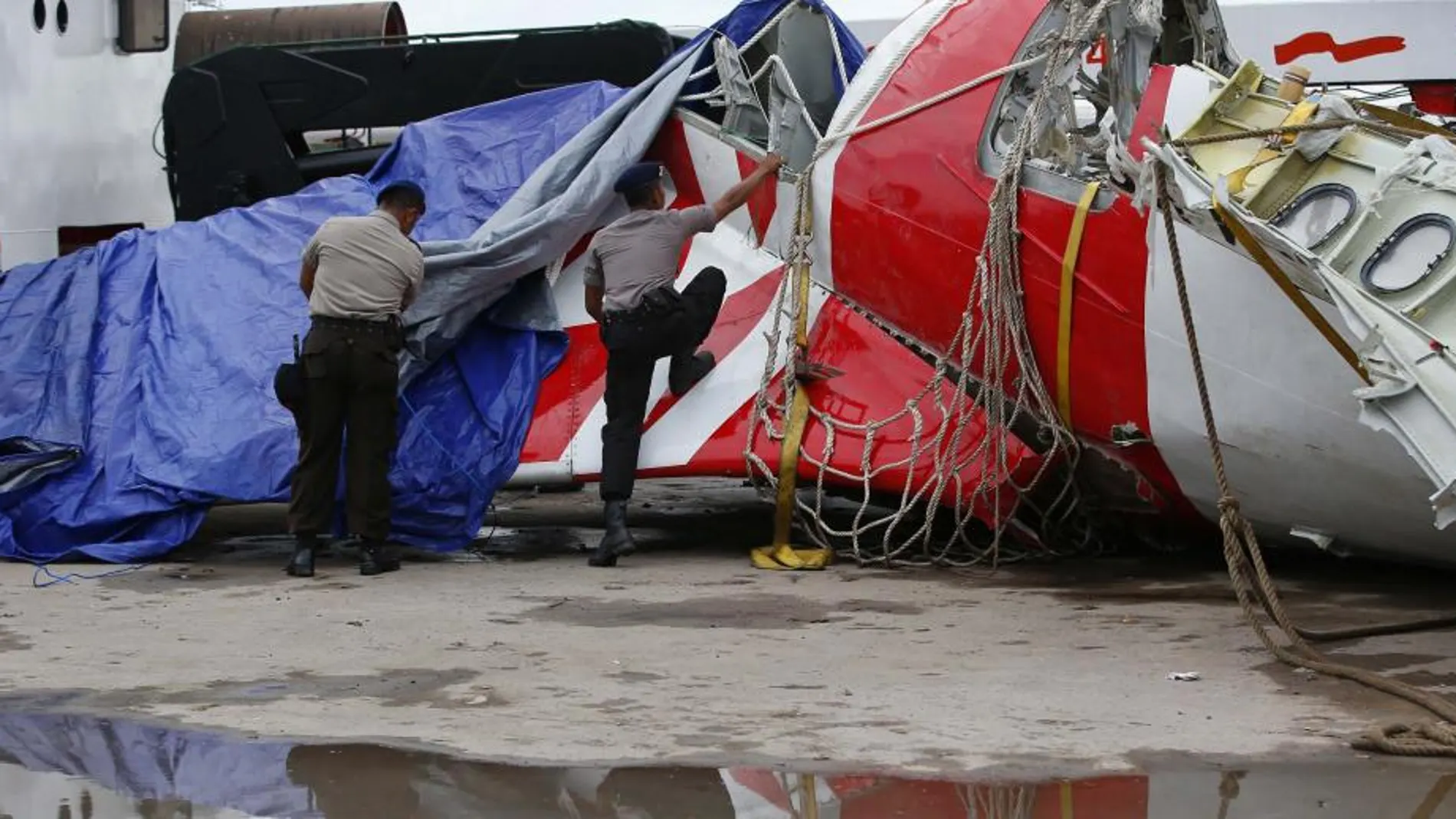 La policía indonesia levanta la lona que cubre la cola del avión