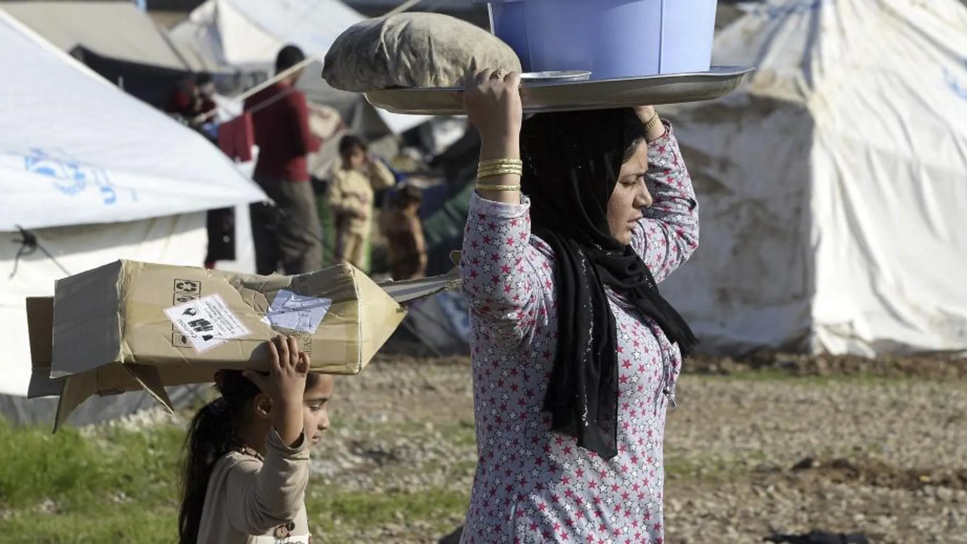 Una mujer yazidí y una niña llevan la colada sosteniéndola en sus cabezas en el campo de refugiados de Baharka, en Irak