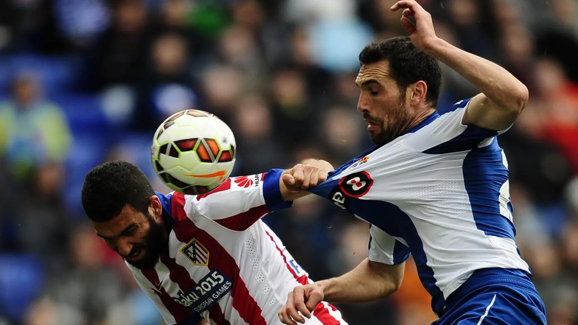 El atlético Arda Turan lucha por un balón y tira de la camiseta al jugador del Espanyol, Anaitz Arbilla