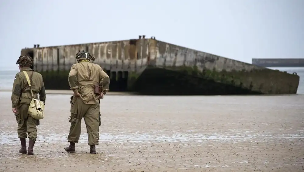 Varios entusiastas de la Segunda Guerra Mundial, con réplicas de uniformes estadounidenses de la época, caminan cerca de las ruinas del pontón de desembarco en la playa de Arromanches, en Normandía, Francia