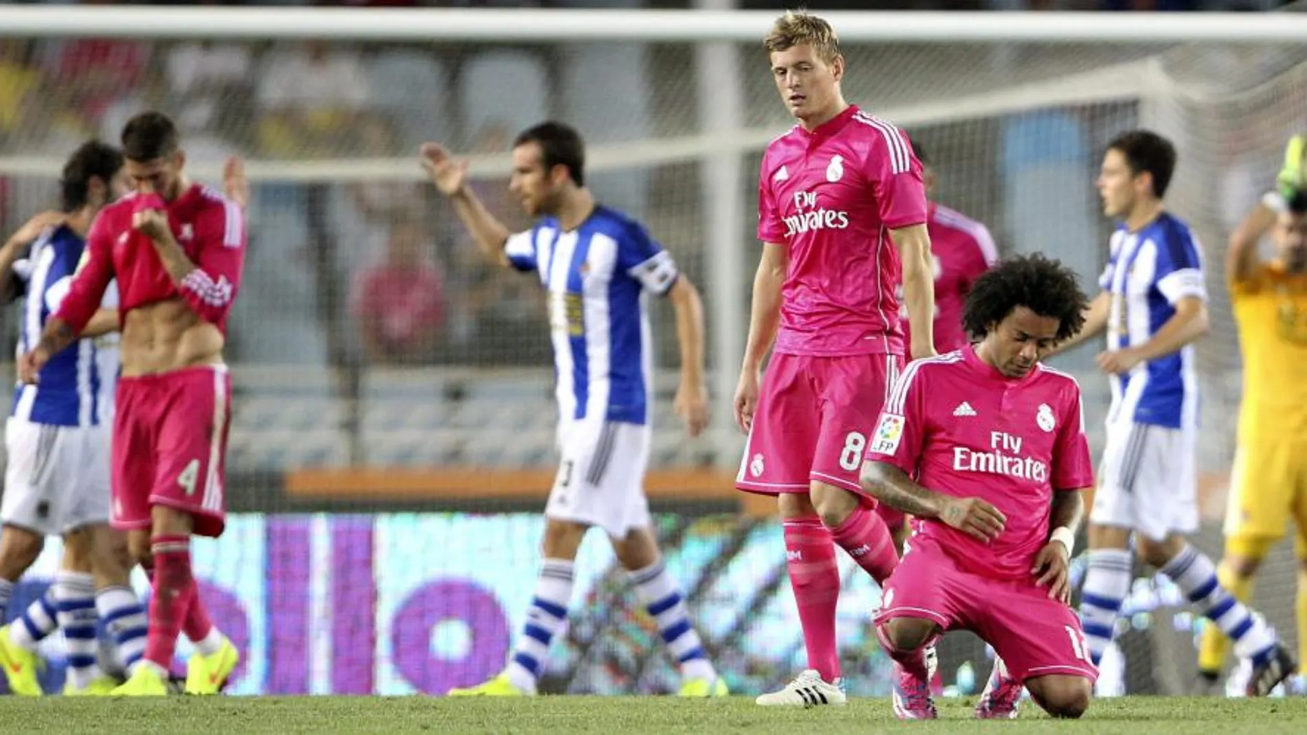 Los jugadores de la Real Sociedad celebran su victoria mientras Marcelo (d), del Real Madrid, se arrodilla al término del encuentro