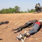 Unos rebeldes fieles a Machar pasan junto a los cadáveres en la cuneta de la carretera hacia el aeropuerto de Bor, a 180 kilómetros de la capital, Yuba