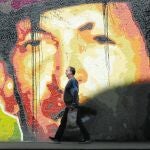 Varios venezolanos caminan delante de un mural de Hugo Chávez