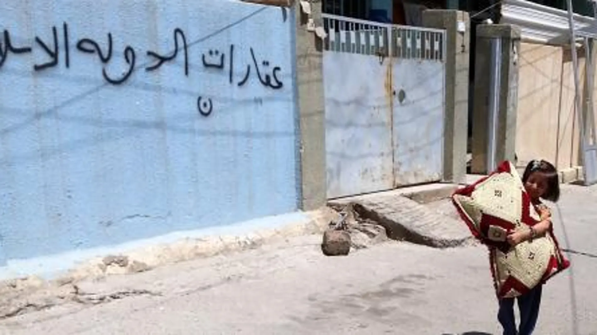 Una niña iraquí mientras camina cerca a una casa desocupada de una familia cristiana, cuyas paredes tienen un grafiti en árabe que dice: "Estado real del Estado Islámico", en la ciudad de Mosul (Irak)