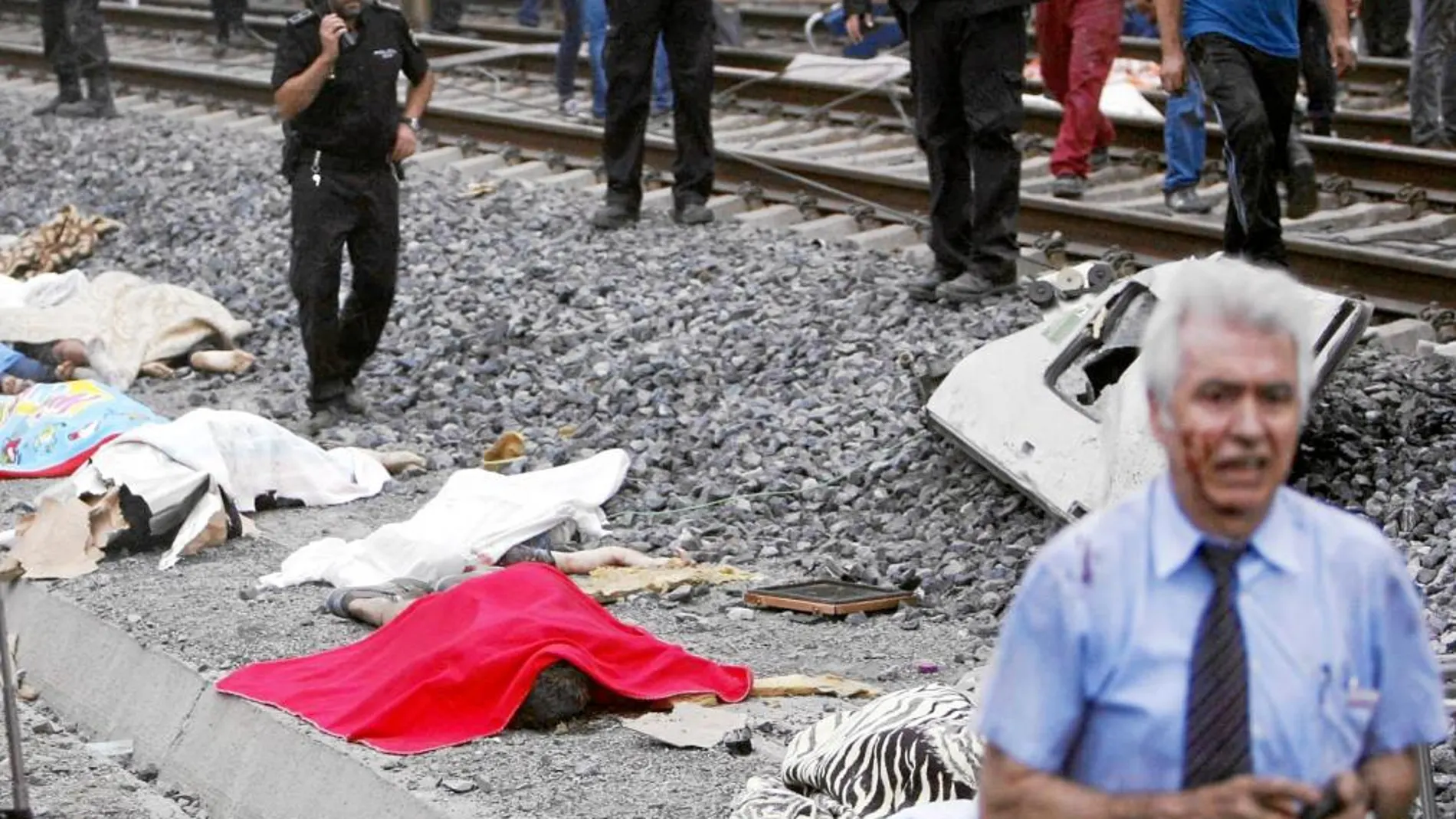 Antonio Martín Marugán, en primer término a la derecha, pasa por delante de algunos cadáveres tras el accidente del miércoles de la semana pasada con su teléfono móvil en las manos