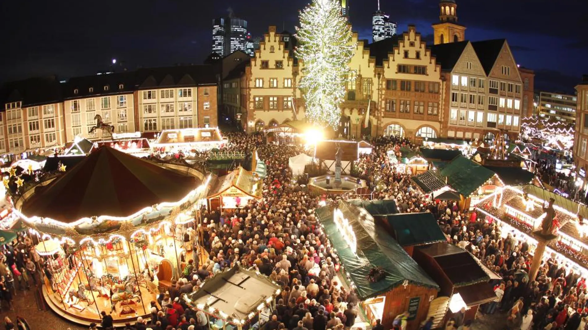 Cientos de personas en un mercadillo navideño de Frankfurt, con un gran árbol de Navidad iluminado.