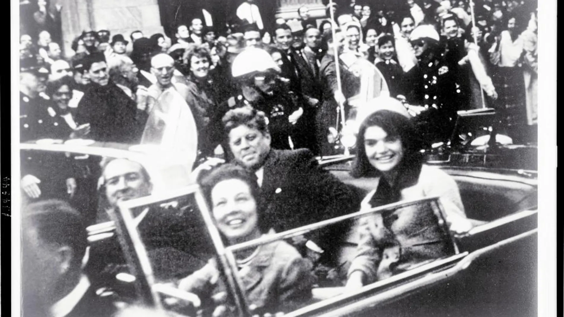 John y Jackie Kennedy sonríen a la cámara durante su paseo por las calles de Dallas, minutos antes del magnicidio