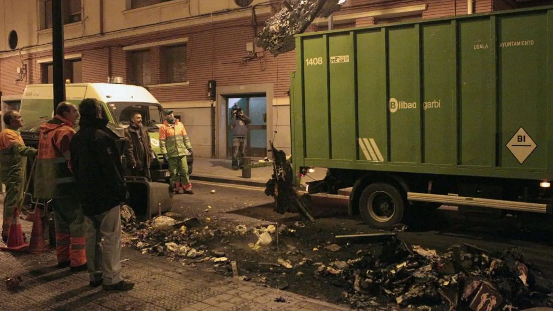Un camión retira uno de los tres contenedores que tres personas encapuchadas han prendido fuego hoy en el barrio bilbaíno de Santutxu.