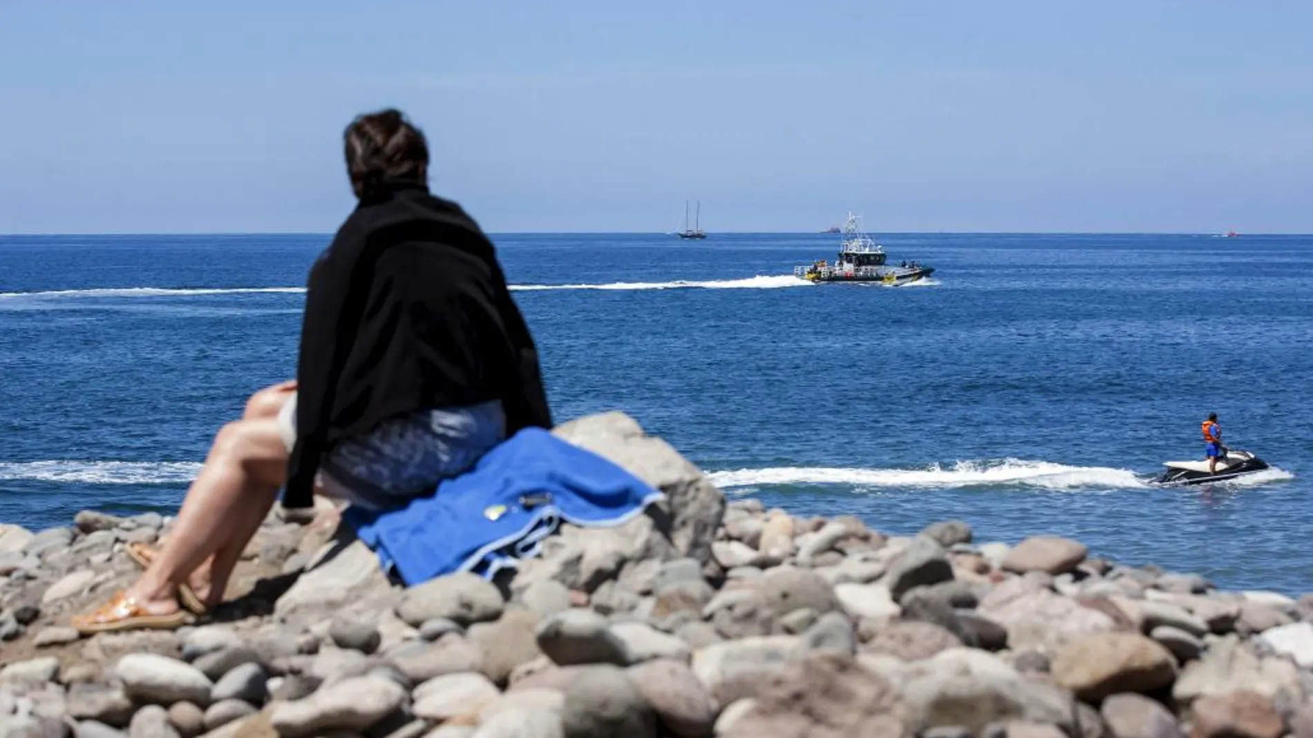 Una patrullera de la Guardia Civil, al fondo, en busca de rastros de fuel en la playa Veneguera, en Gran Canaria
