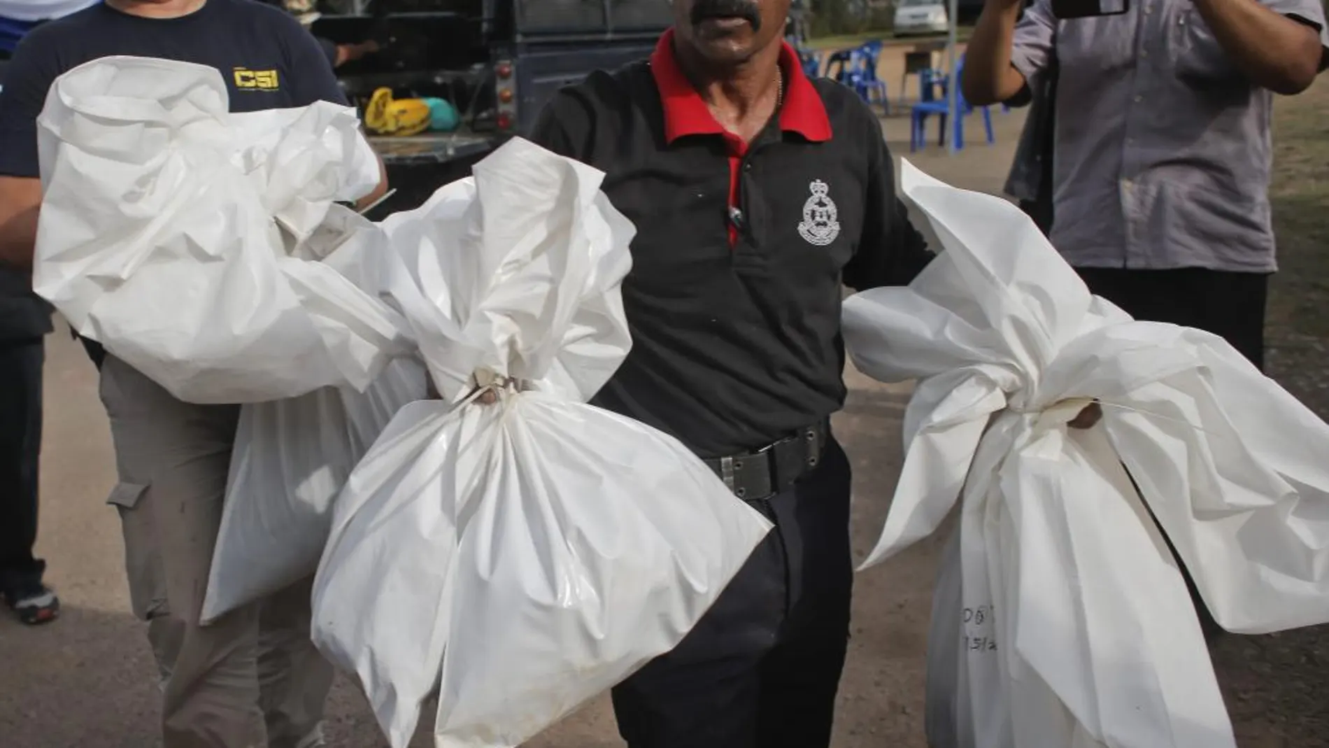 Un policía malasio se hace cargo de unas bolsas que contienen restos humanos en Wang Kelian (Malasia).