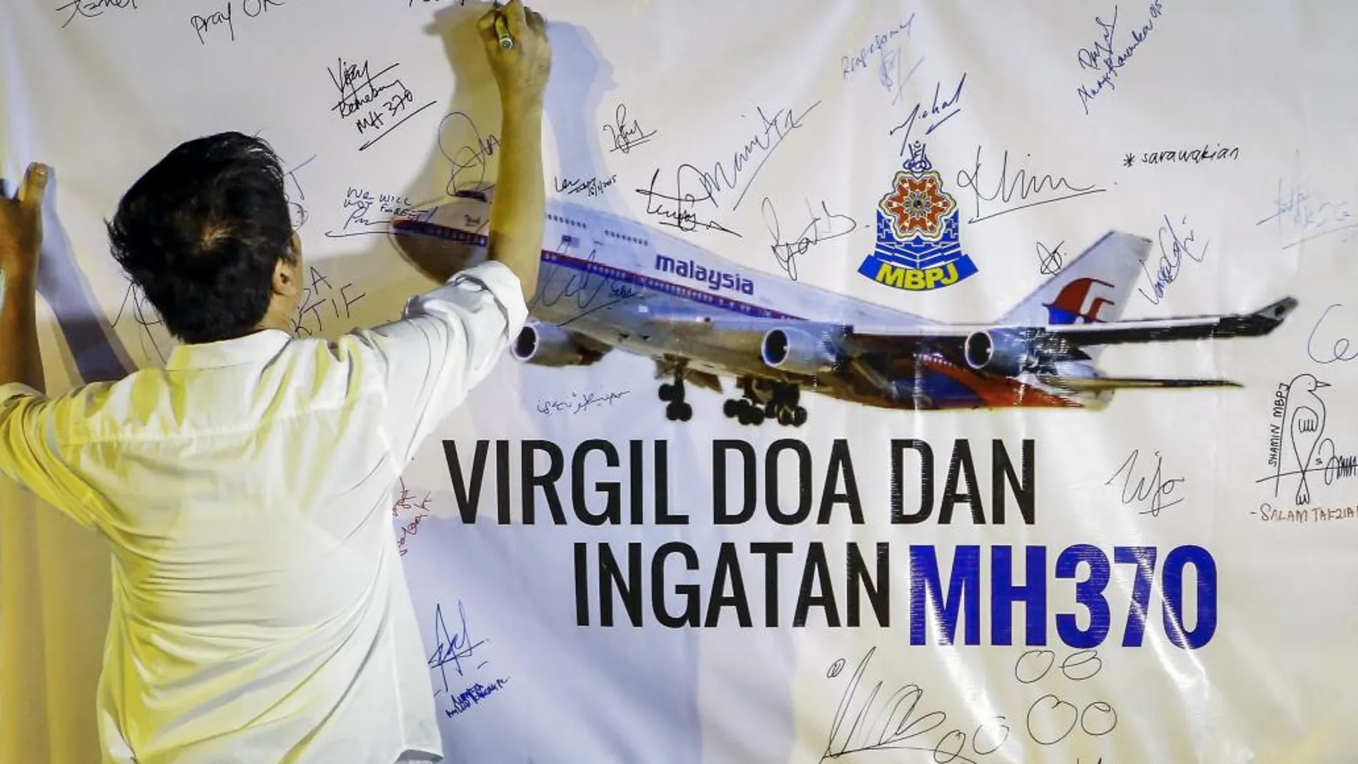 Un hombre escribe un mensaje en un mural durante un acto en recuerdo de las víctimas del vuelo MH370 de Malaysian Airlines.