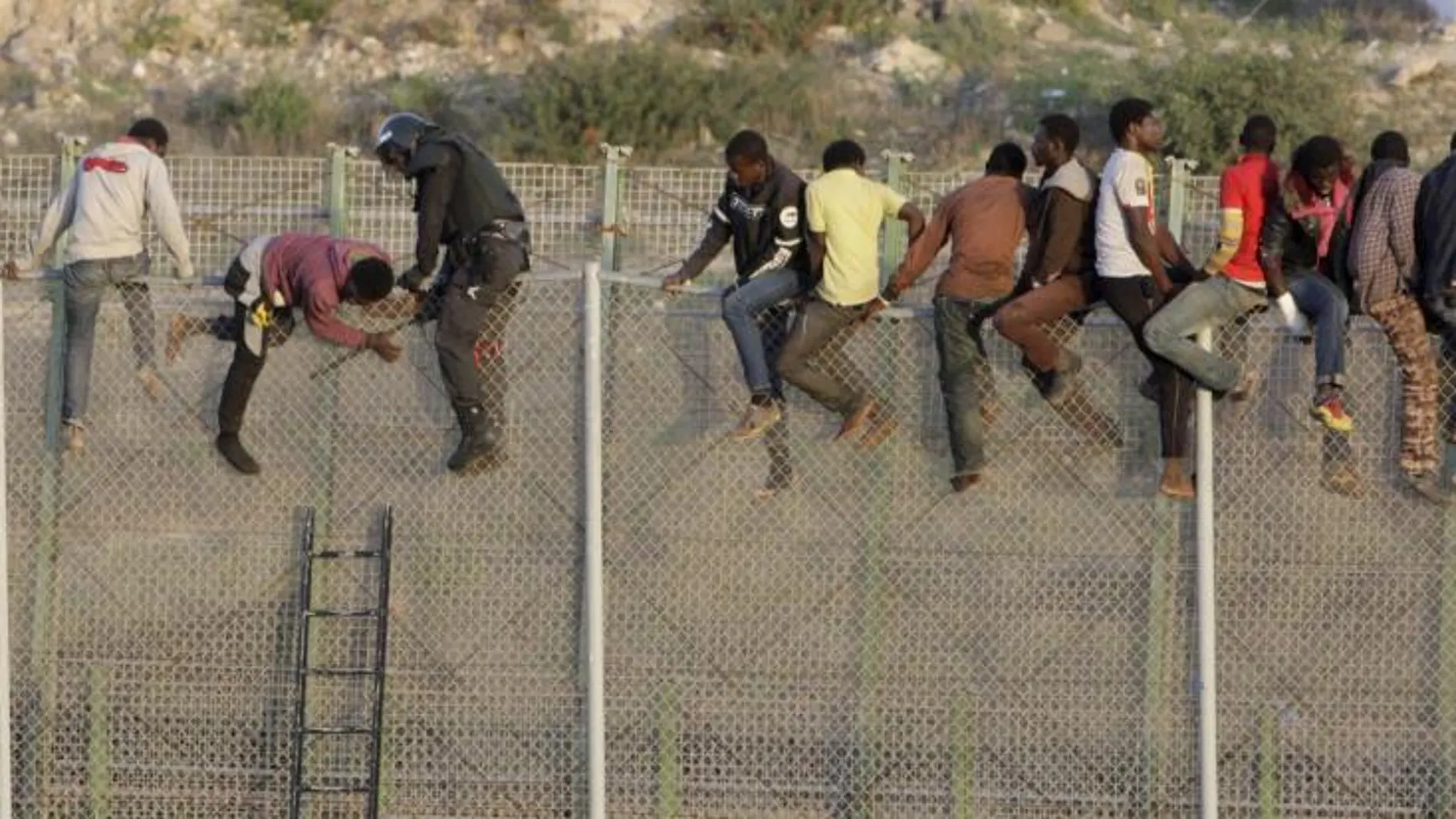 Agentes de Policía junto a a algunos inmigrantes encaramados a la valla de Melilla, en una imagen de octubre