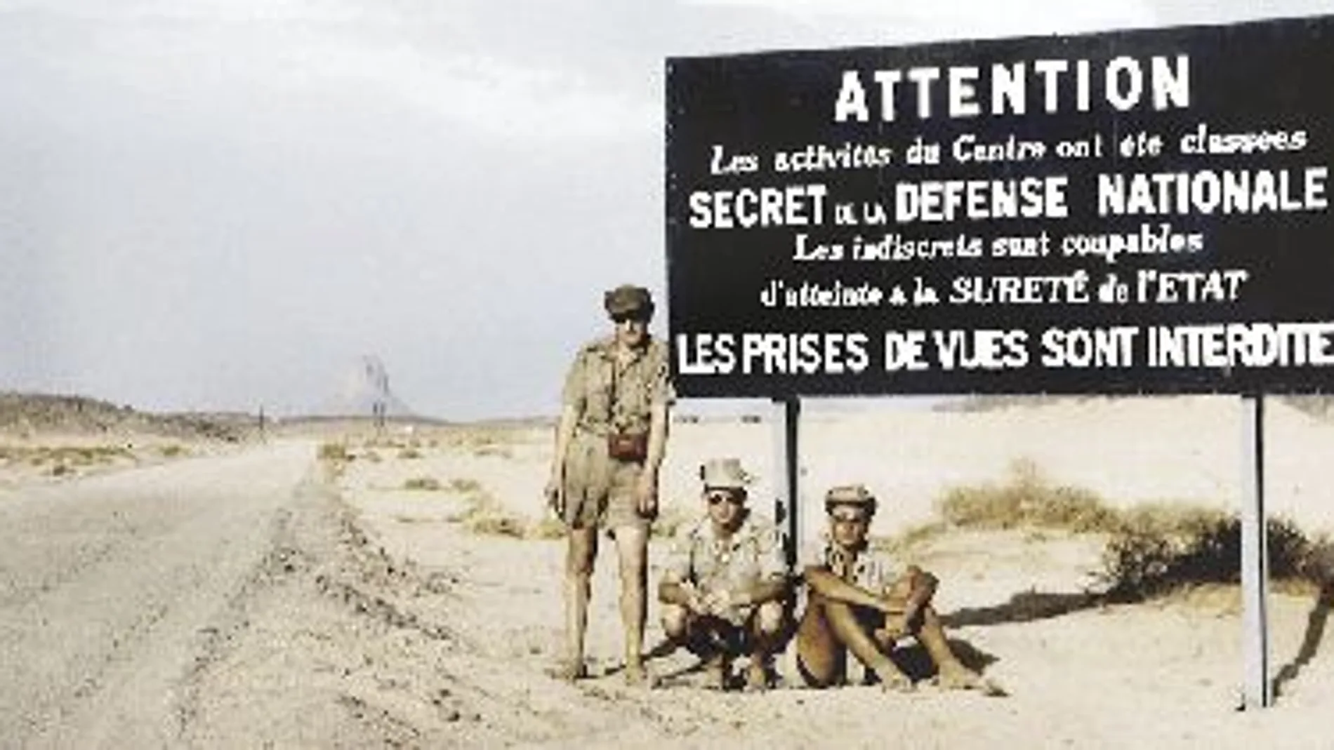 Pierre Leroy, junto otros compañeros, ante el cartel que prohibe el paso y realizar fotografías en zona de pruebas atómicas en el Sáhara argelino