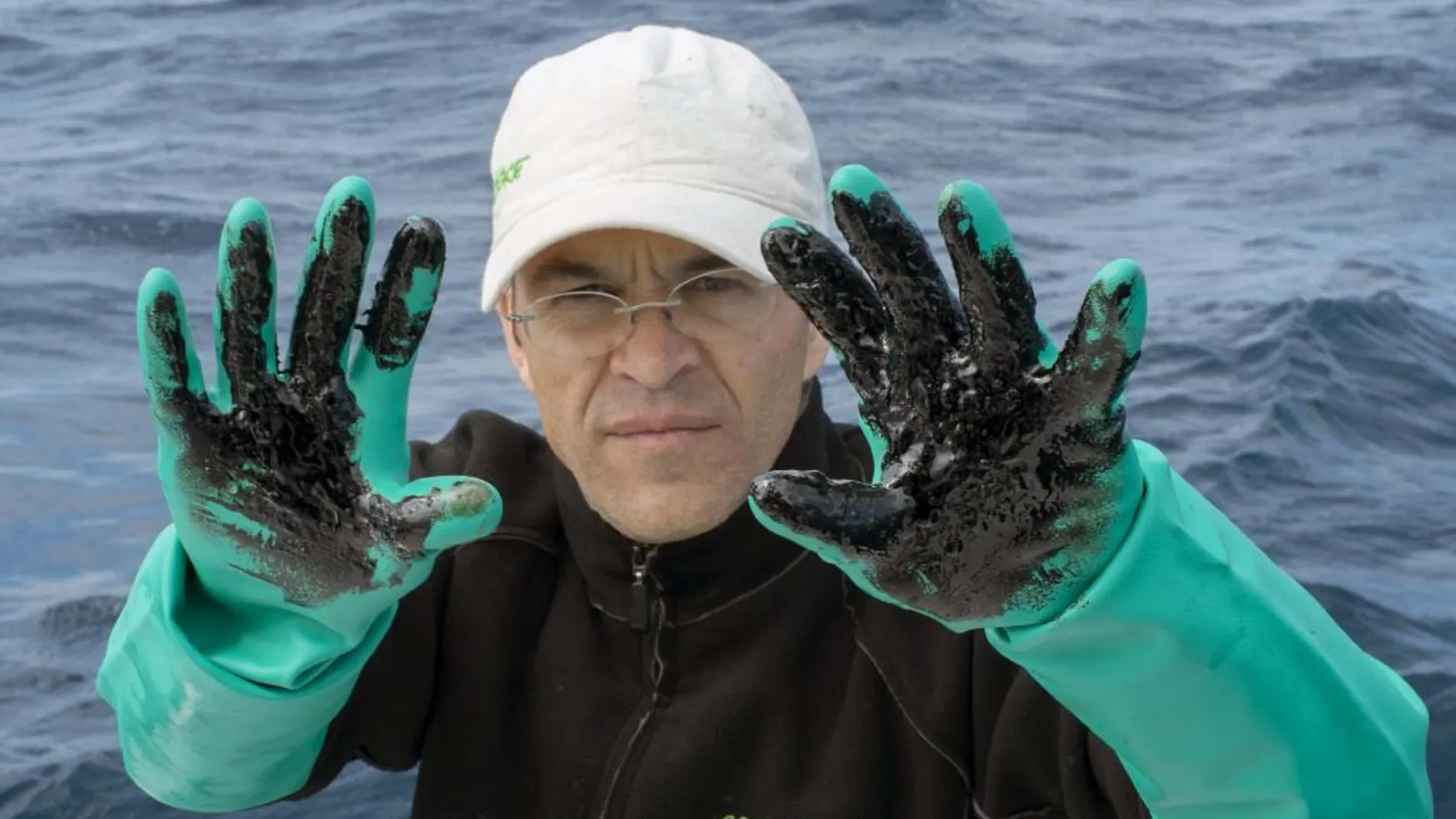 Un activista de Greenpeace muestra sus manchadas de fuel en el lugar del hundimiento