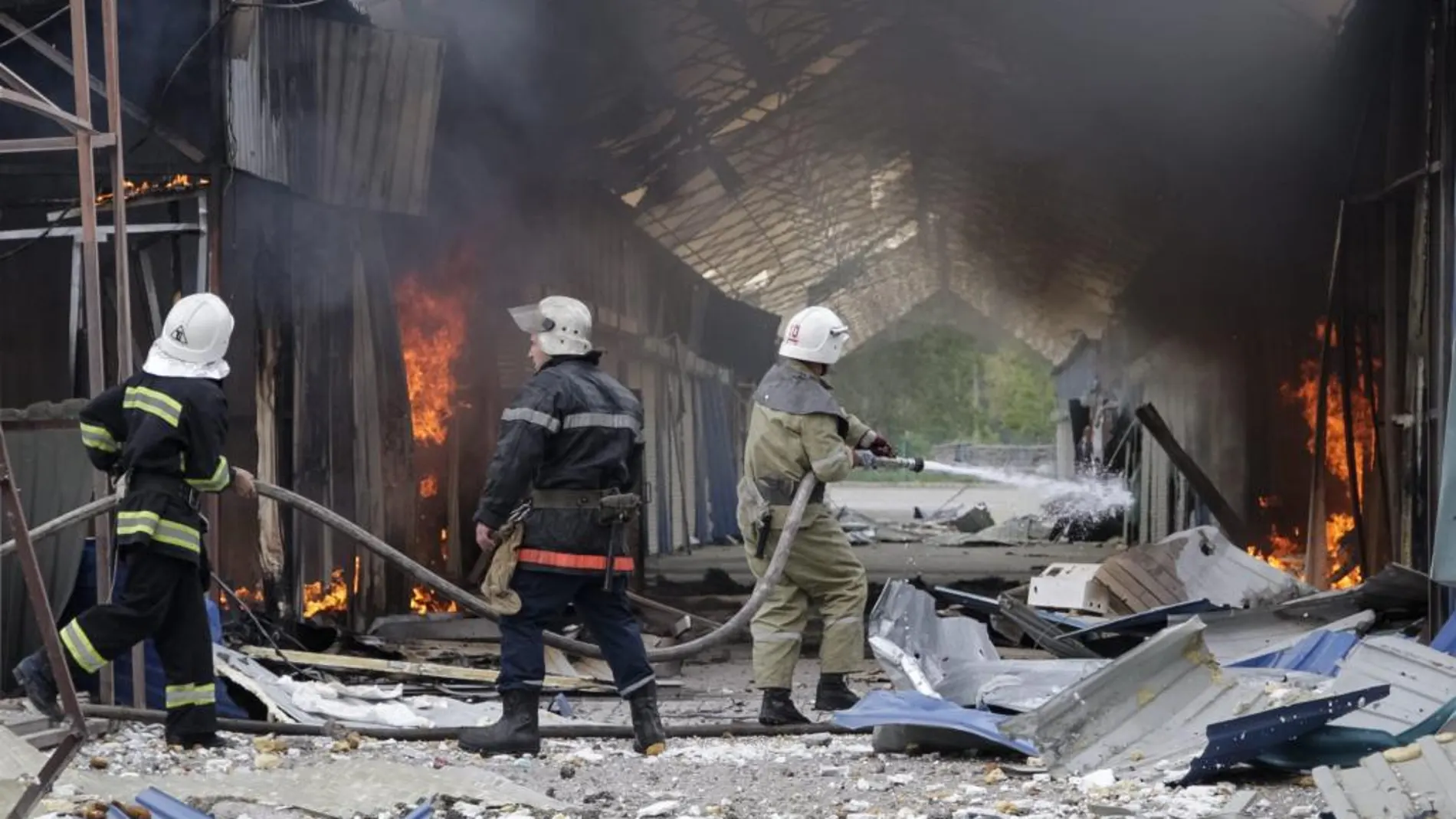 Varios bomberos trabajan en las labores de extinción de un incendio en un centro comercial tras un bombardeo a las afueras de Donetsk, Ucrania