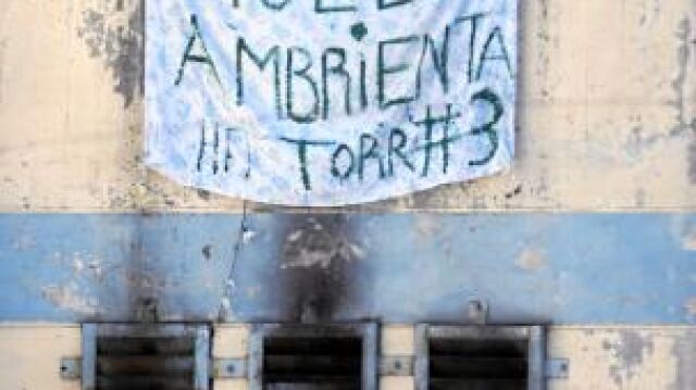 Un recluso saluda en las celdas cercanas al lugar donde murieron 81 presos entre carteles de protesta por la situación del presidio
