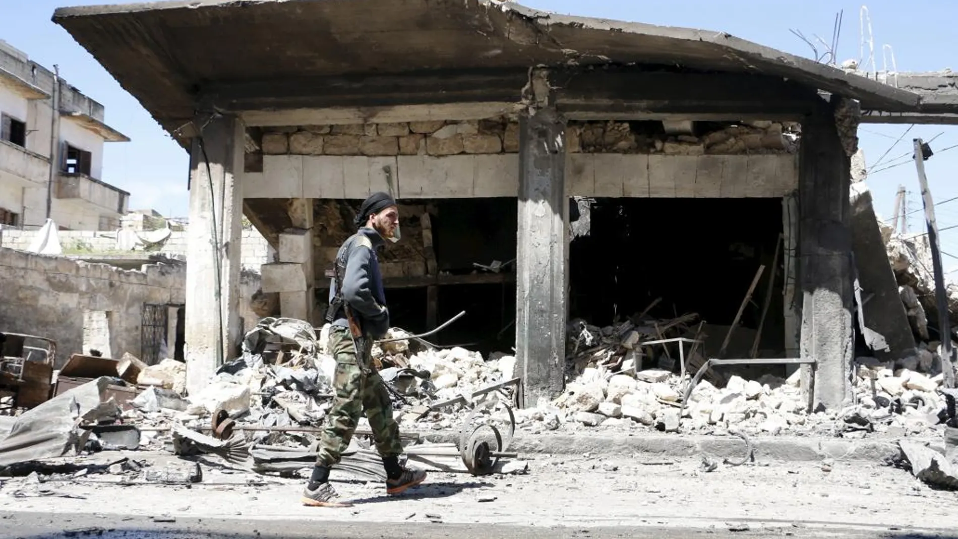 Un miembro del Al Qaeda pasa junto a una casa destruida por los bombardeos