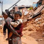 Una mujer nepalí lleva a cuestas a su hijo en una carretera destruida por el terremoto en Sindhupalchowk