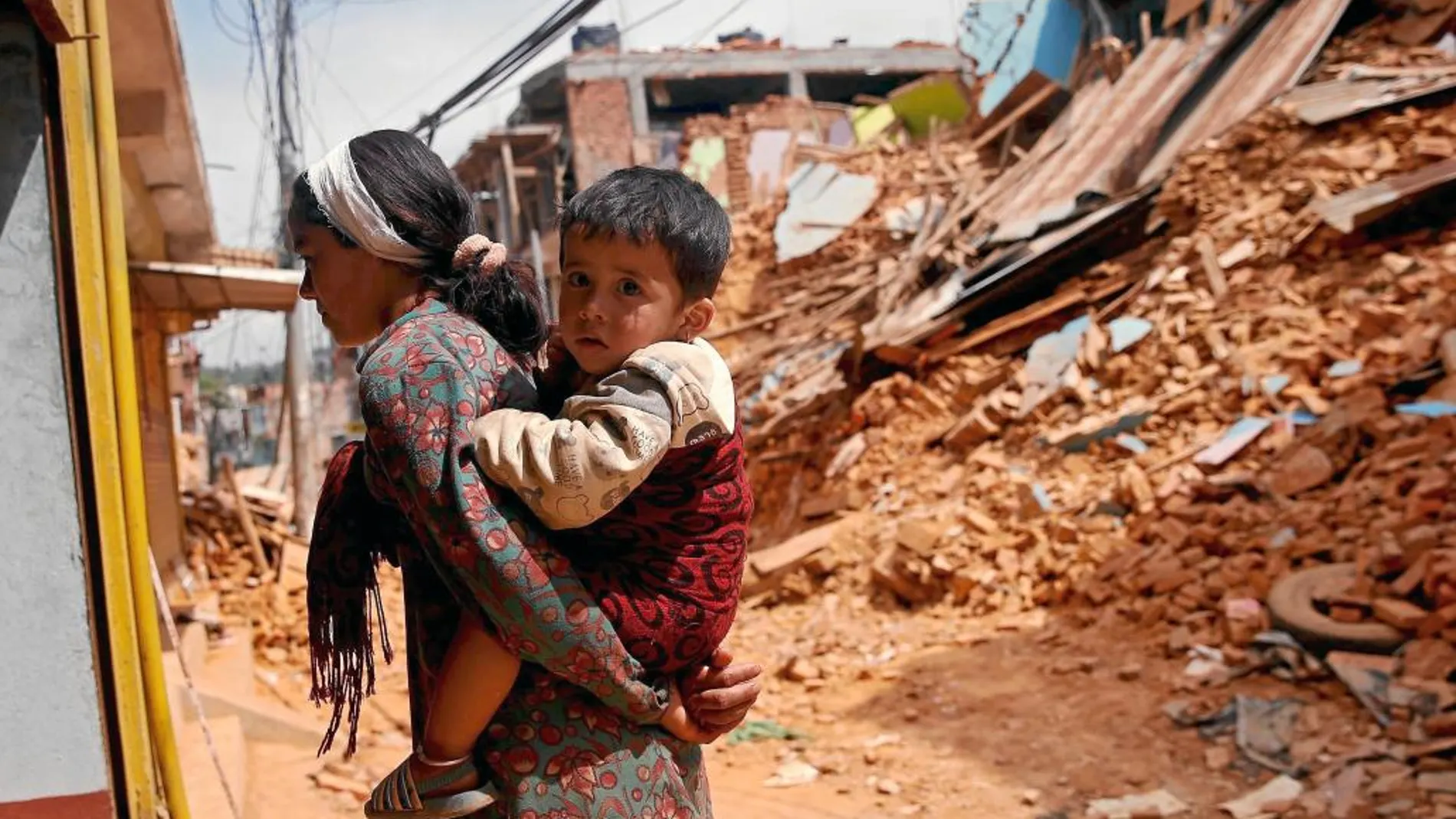 Una mujer nepalí lleva a cuestas a su hijo en una carretera destruida por el terremoto en Sindhupalchowk
