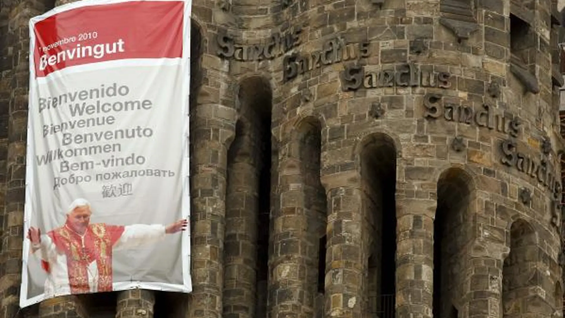 Detalle del cartel colgado en una de las torres de la fachada del Nacimiento de la Sagrada Familia en el que se da la bienvenida al Papa en varios idiomas