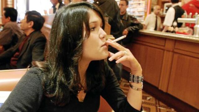 Una chica fuma un cigarrillo en un bar, mientras espera que el camarero le sirva