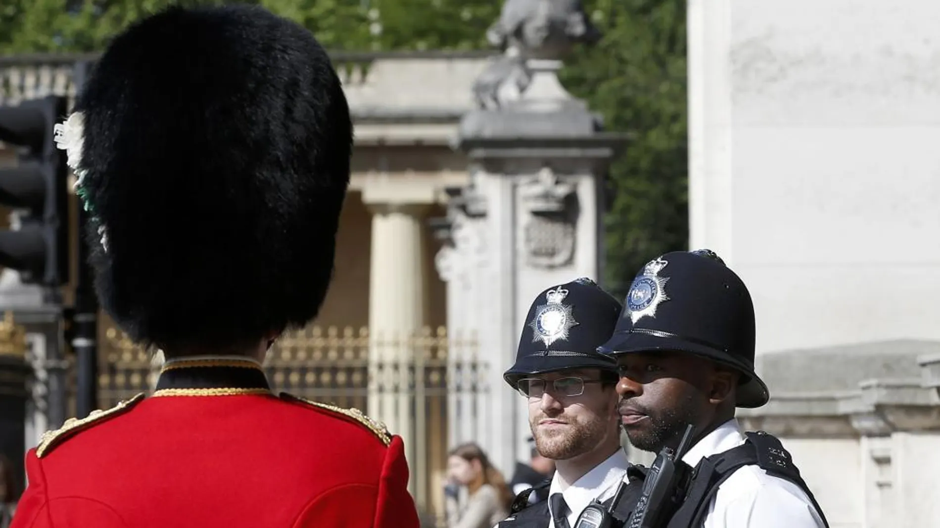 Dos policías londinenses conversan con un gudia de Buckingham Palace