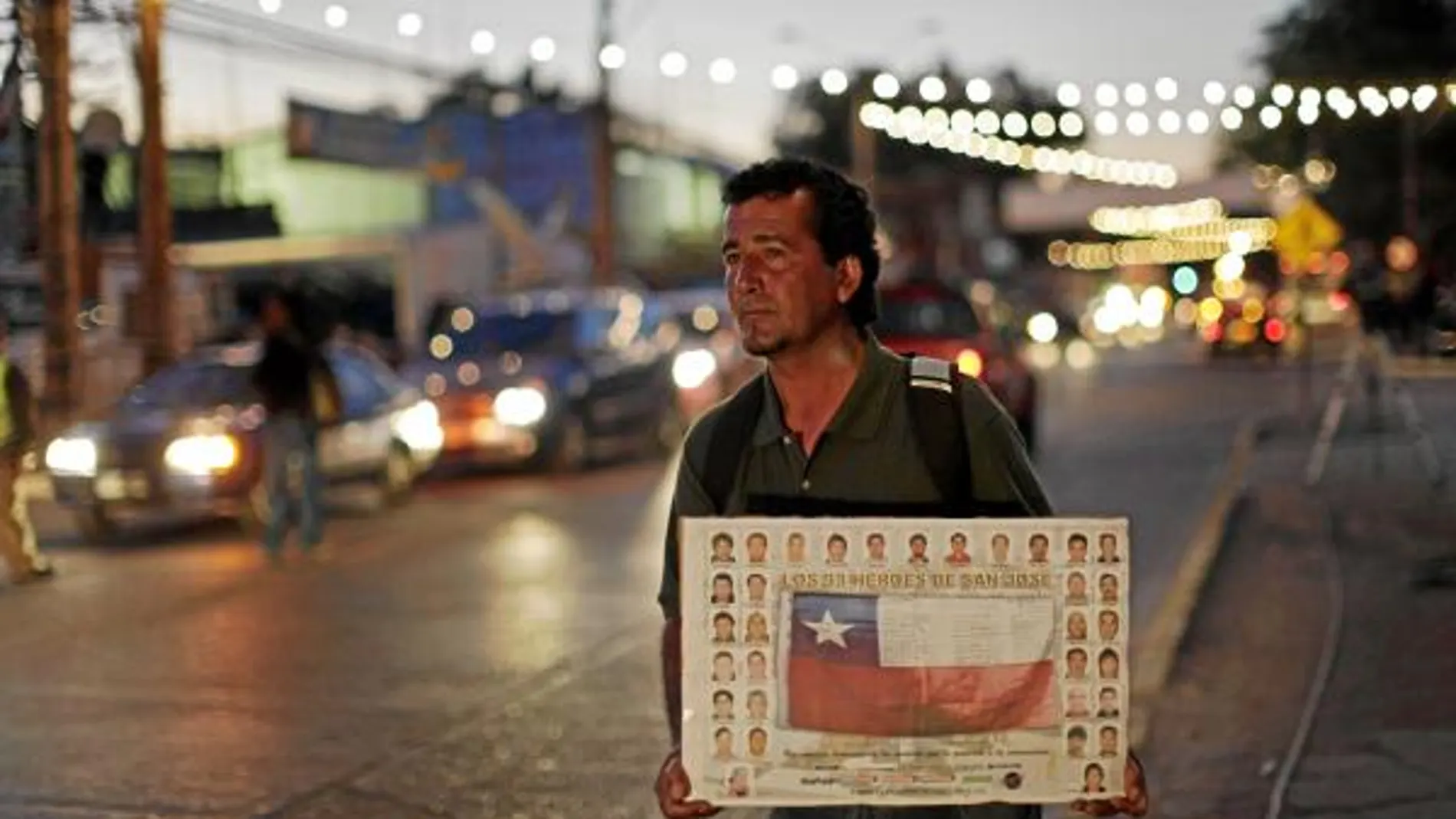 Un hombre sujeta un cartel con la bandera chilena y los rostros de los 33 mineros cerca del Hospital de Copiapó