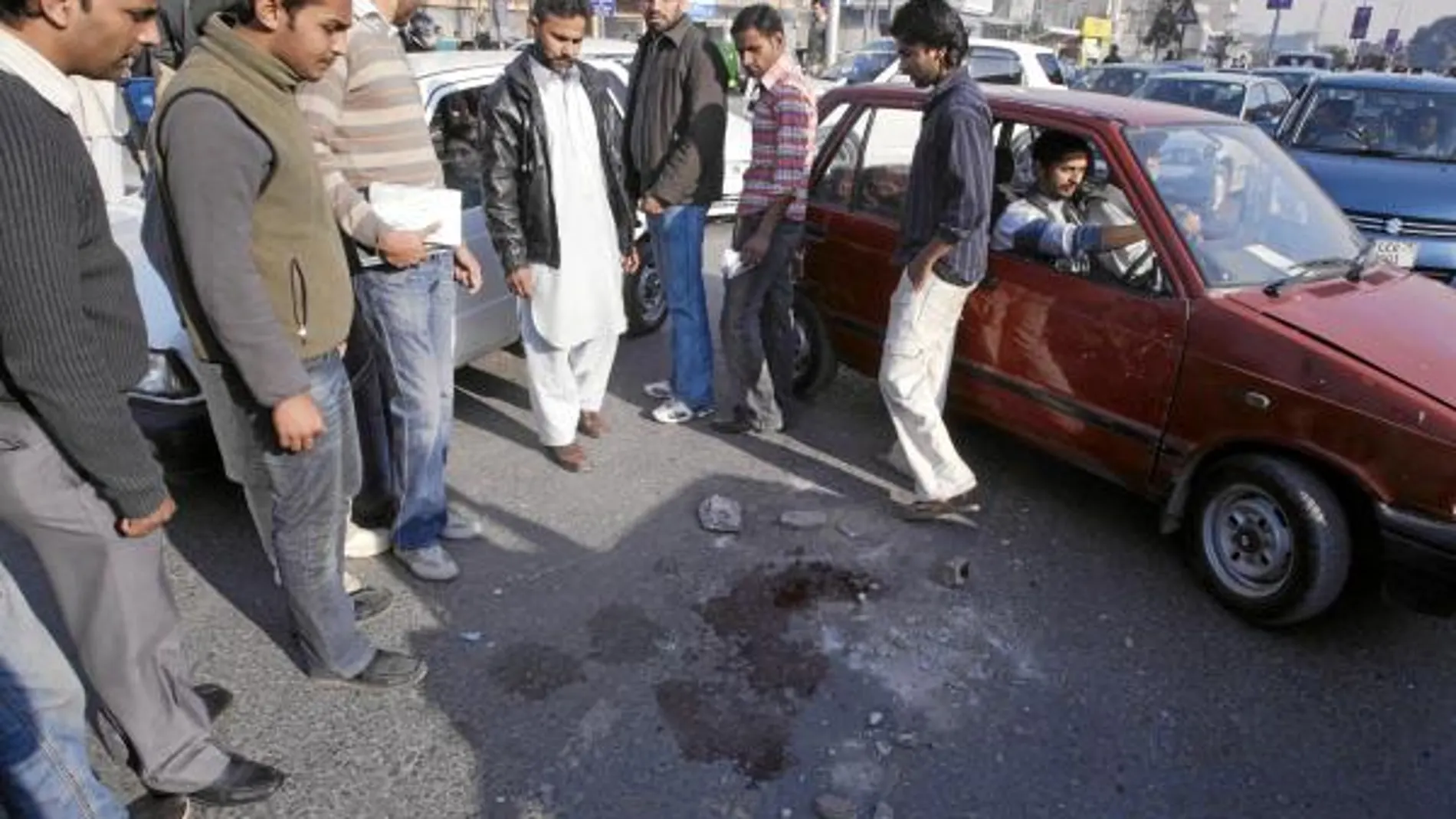Varios hombres observan los restos de sangre en el lugar donde se produjo el tiroteo, en una calle de Lahore
