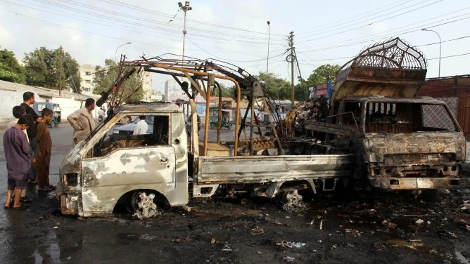 Un grupo de jóvenes curiosea junto a los restos de dos vehículos incendiados durante los incidentes para protestar contra los atentados en Karachi
