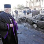 Un sacerdote iraquí contempla los restos de un coche utilizado para cometer un atentado suicida en Bagdad