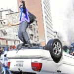 Un estudiante chileno salta sobre un coche volcado en una calle de Santiago