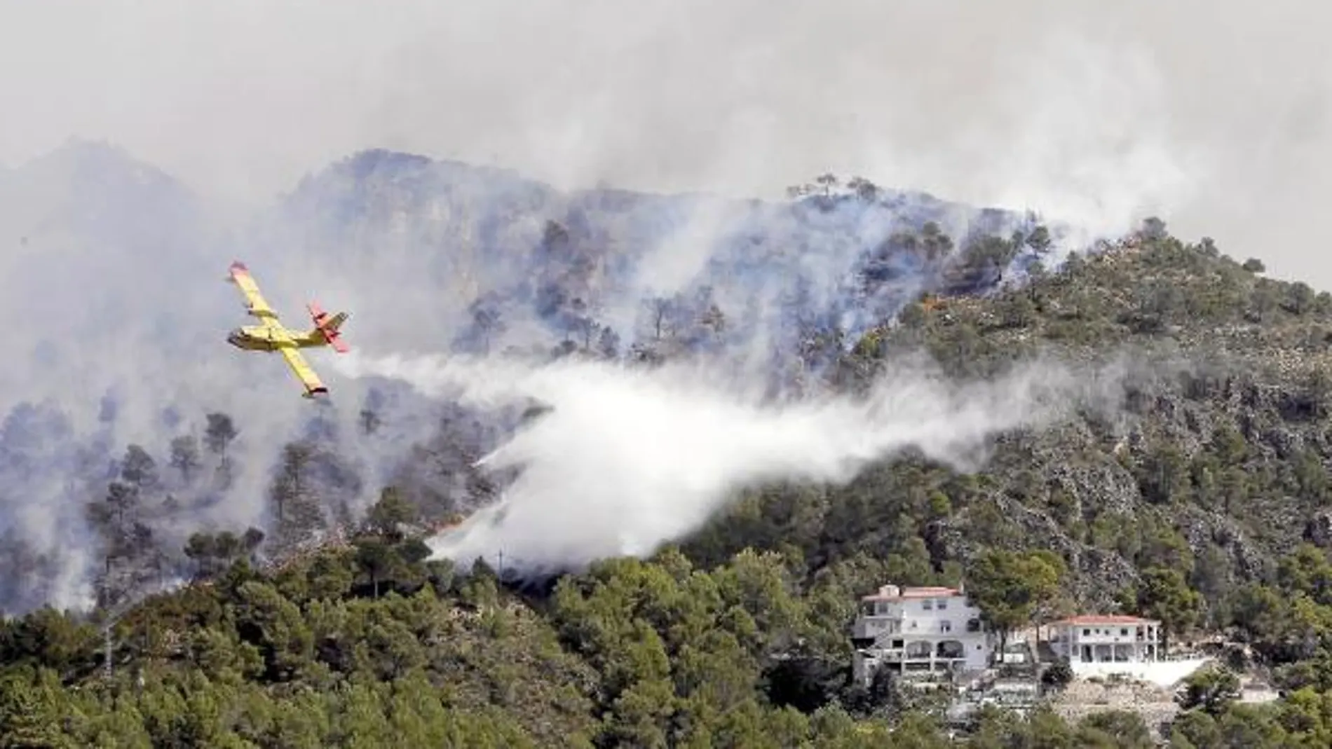 Un hidroavión arroja agua sobre una zona de viviendas afectadas por el incendio de Benicolet y Almisserat