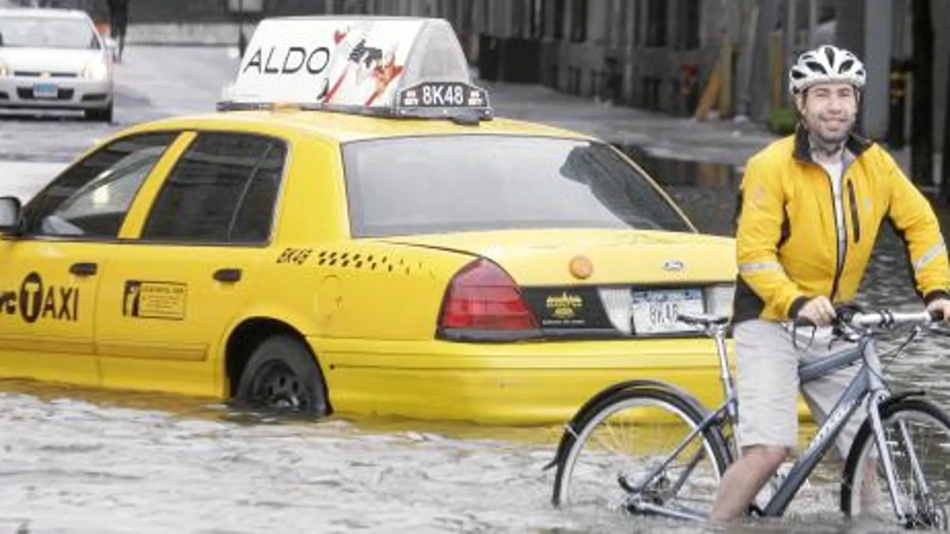 Un ciclista intenta avanzar en una calle inundada de Nueva York, ayer, junto a un taxi inmovilizado por el agua