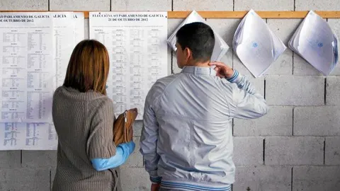Dos jóvenes gallegos comprueban las listas del censo electoral para saber en qué mesa les corresponde votar