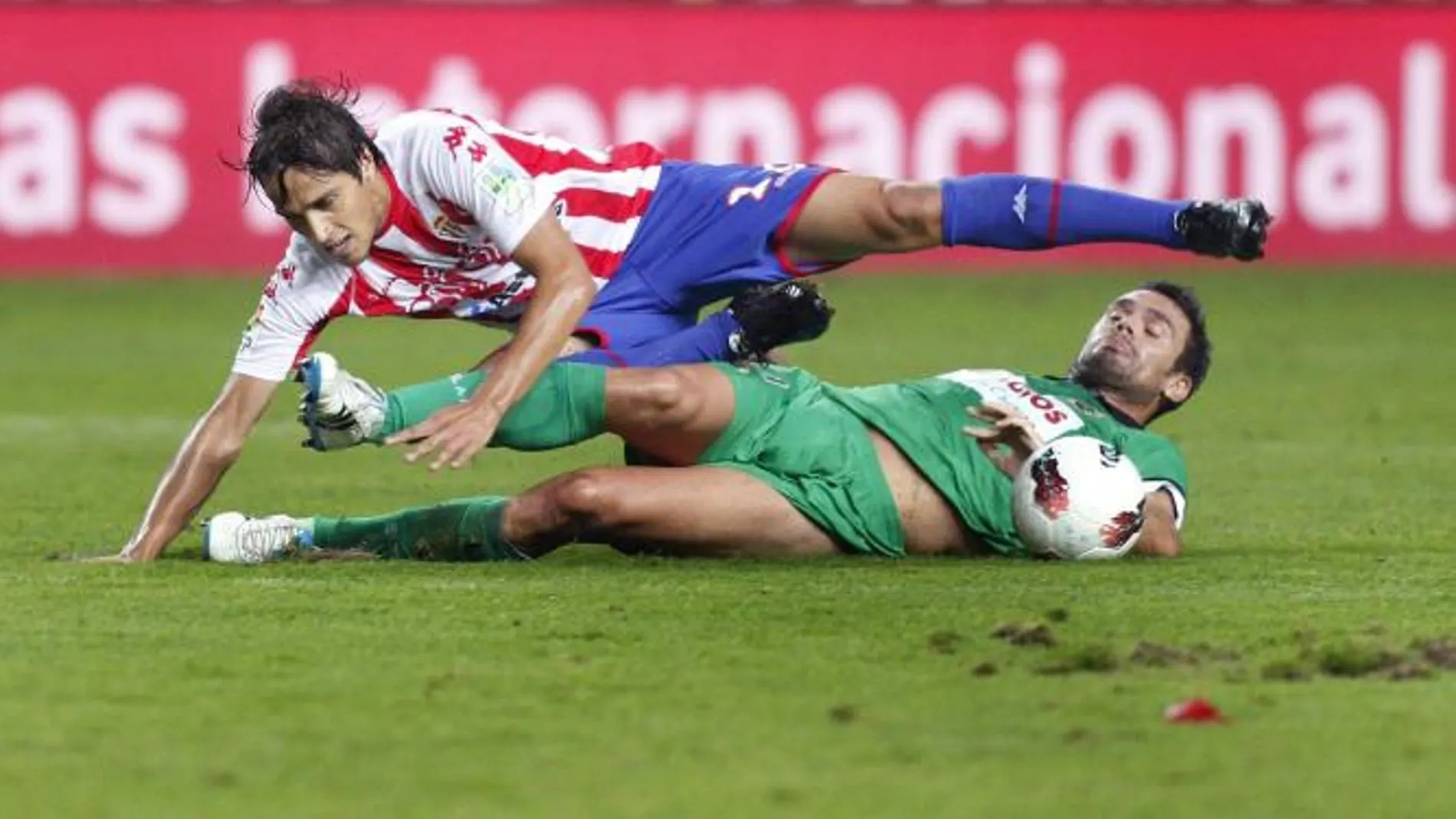 El delantero argentino del Sporting de Gijón Oscar Trejo (encima) cae en presencia del centrocampista griego del Racing de Santander Alexandros Tziolis
