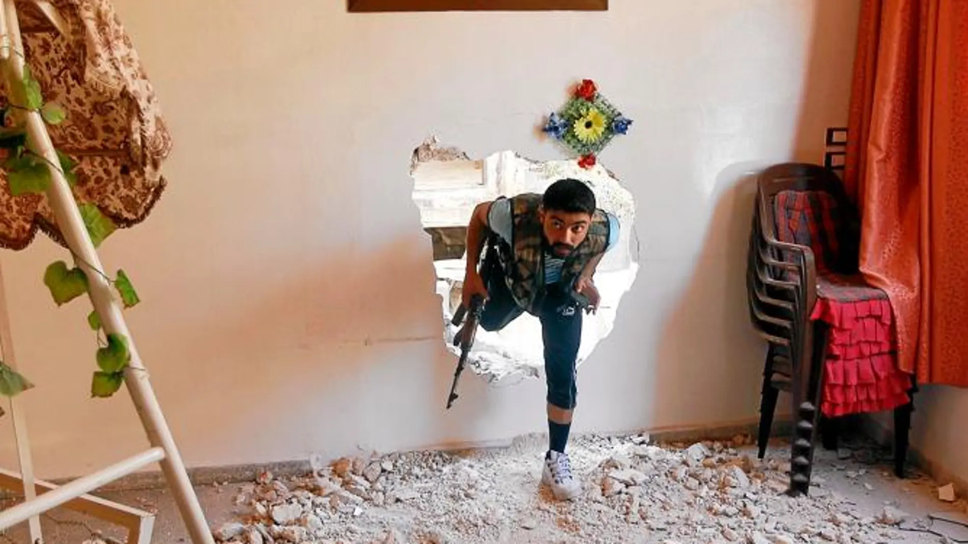 Un rebelde sirio entra a un edificio por un agujero en la pared para protegerse de los bombardeos en Alepo