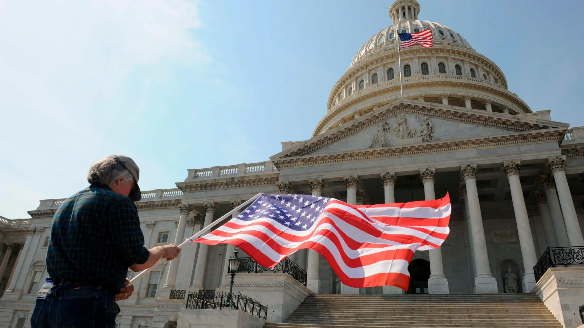 Un hombre con una bandera de los Estados Unidos delante del Capitolio en Washington