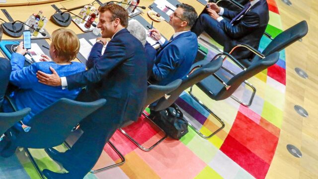 Angela Merkel consulta su móvil mientras charla con Emmanuel Macron ayer en la cumbre de Bruselas