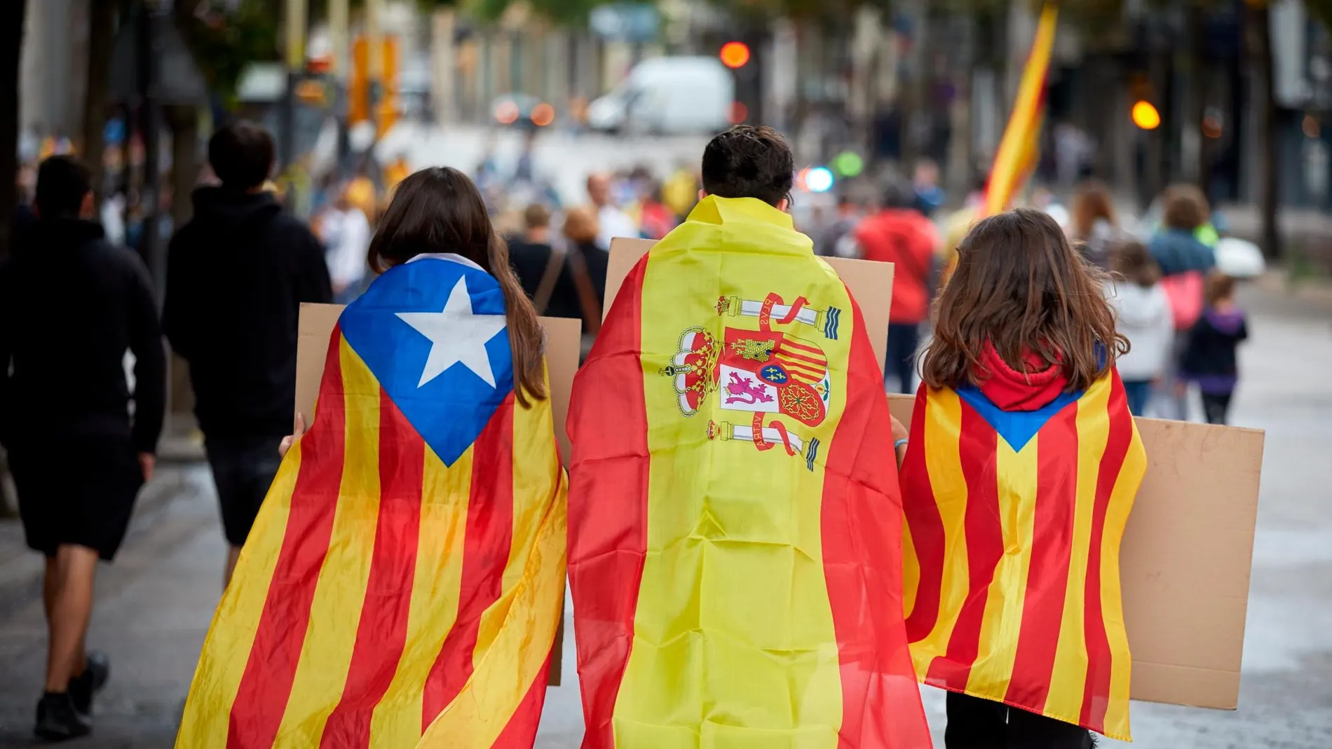 Tres jóvenes ataviados con banderas de España y esteladas se dirigen a la manifestación en la que miles de personas recorren las calles de Girona