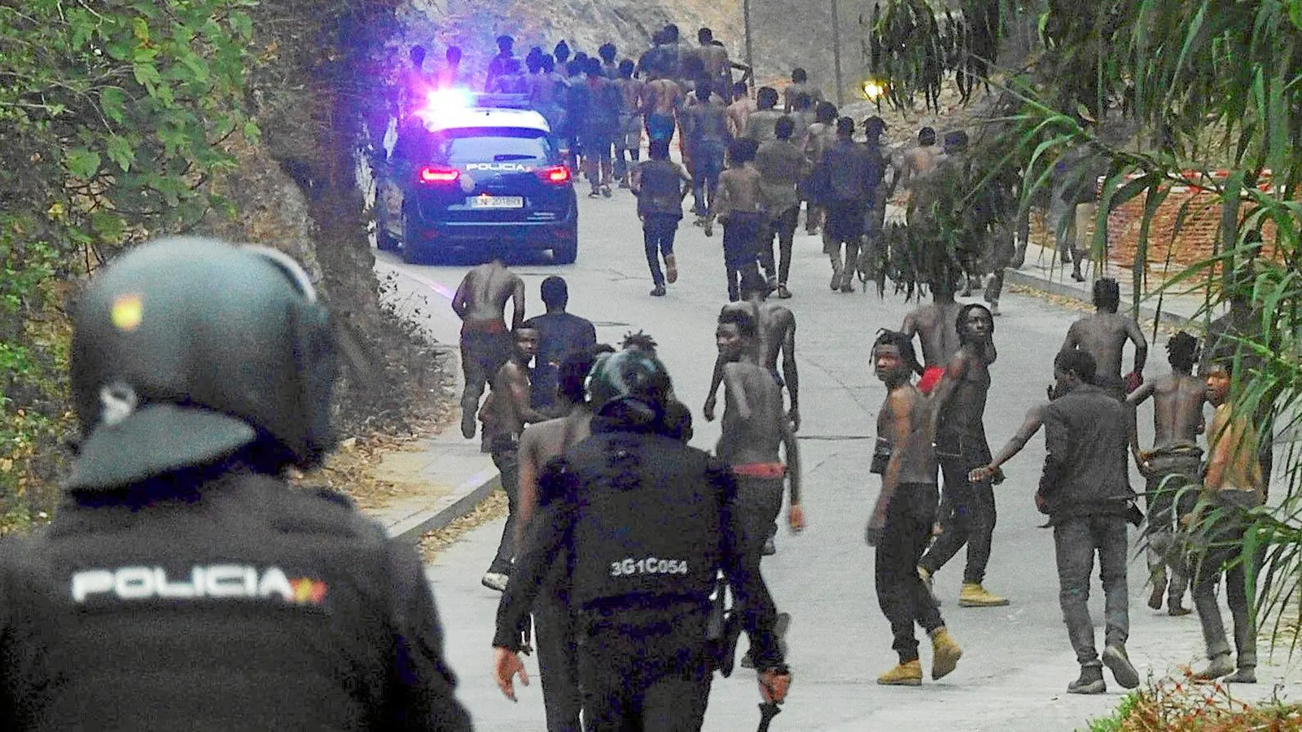 Agentes de la policía corren tras los inmigrantes tras la entrada en Ceuta. El salto a la valla fue uno de los más violentos y el primero desde el mes de agosto del año pasado